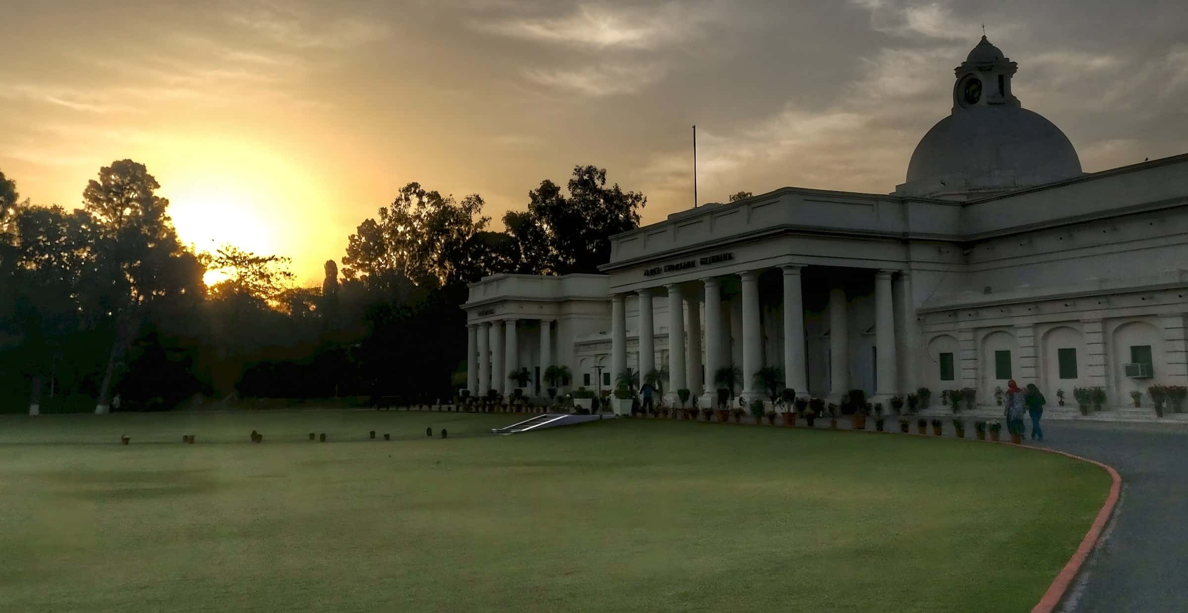 The sun rising behind trees beside the domed Main Building.