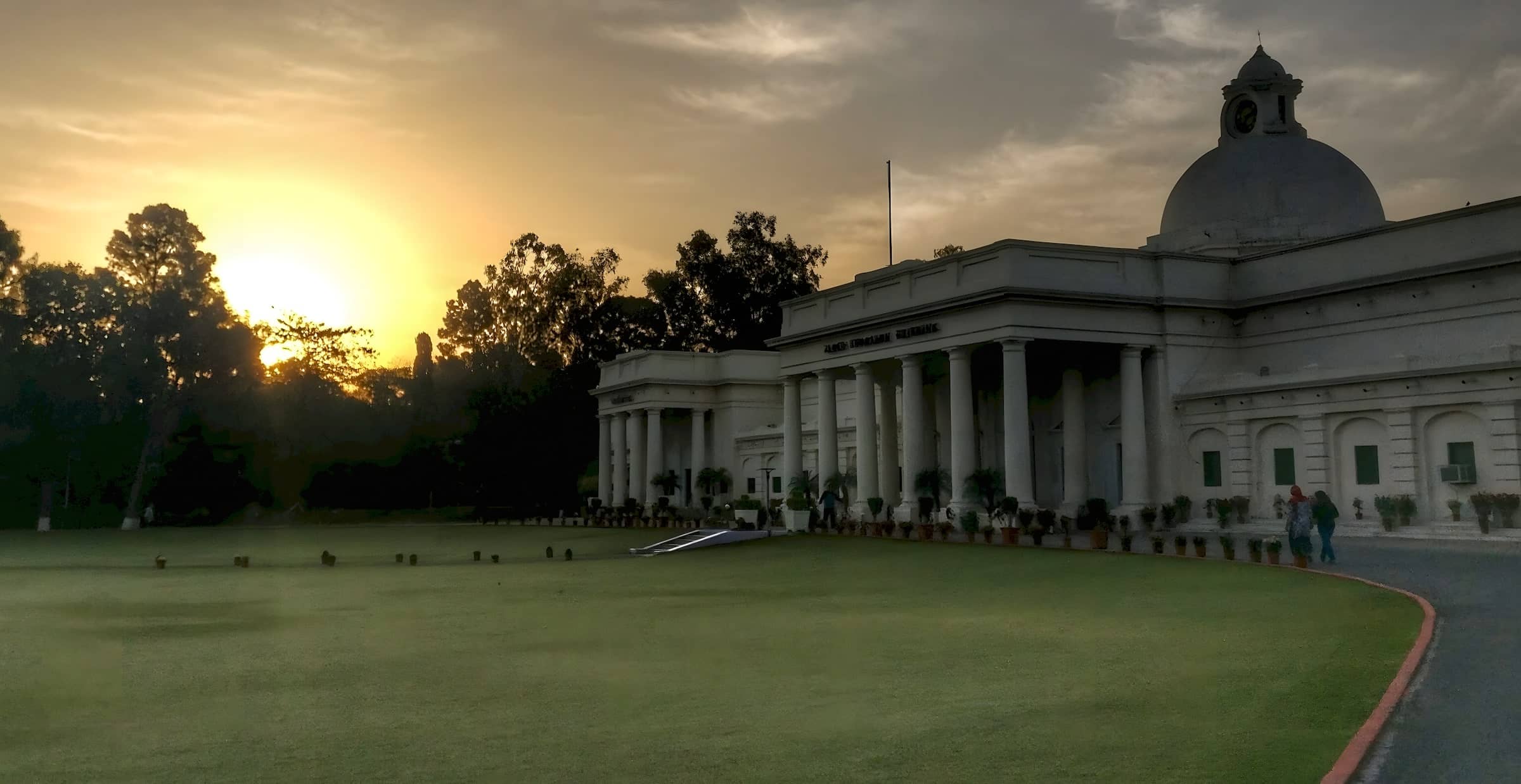 The sun setting behind trees beside the domed Main Building at IIT Roorkee.